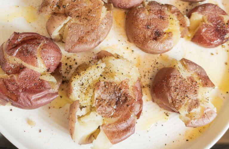 smash potatoes on white plate with olive oil salt and pepper