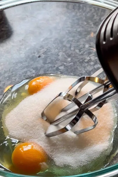 glass bowl with eggs and sugar and beater for almond flour chocolate zucchini muffins