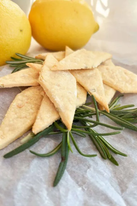 A stack of crispy gluten-free lemon rosemary sourdough discard crackers with a sprig of rosemary