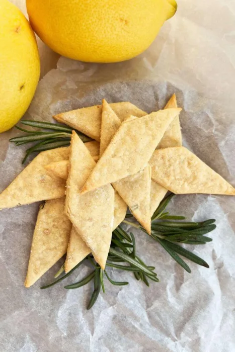 A stack of gluten-free lemon rosemary sourdough discard crackers with fresh rosemary sprigs and lemons