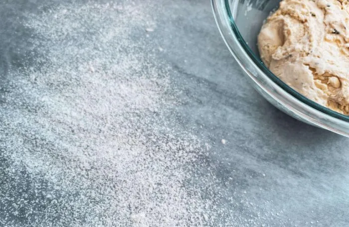 Gluten-free lemon rosemary sourdough discard cracker dough in a bowl beside flour dusted parchment paper