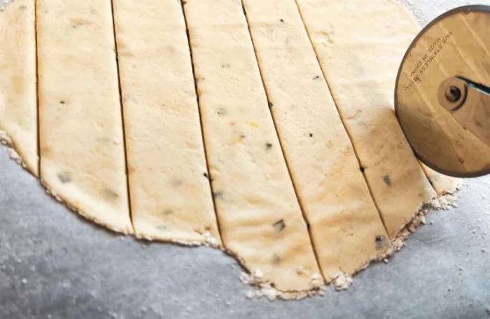 Gluten-free lemon rosemary sourdough discard cracker dough rolled out being cut with a pizza cutter 