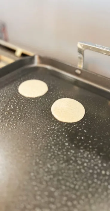 Pouring gluten-free sourdough discard pancake batter onto a hot skillet for cooking