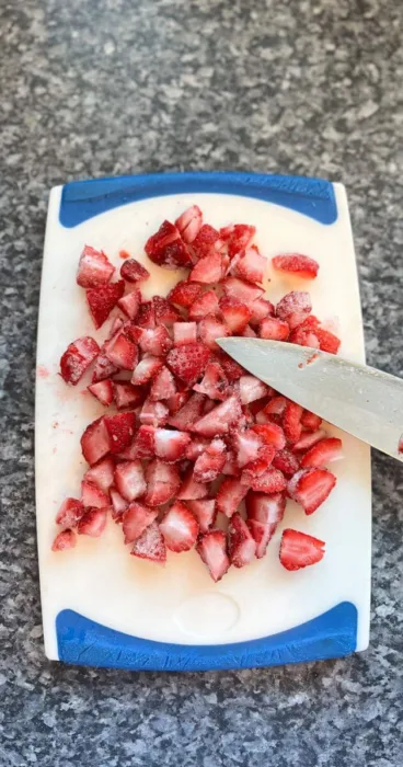 A close-up of frozen strawberries being cut for the silky gluten-free strawberry sauce, showcasing the process of making this delicious condiment.