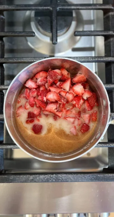 Frozen strawberries being added to the cooking pot on the stovetop for preparation of gluten-free strawberry sauce.