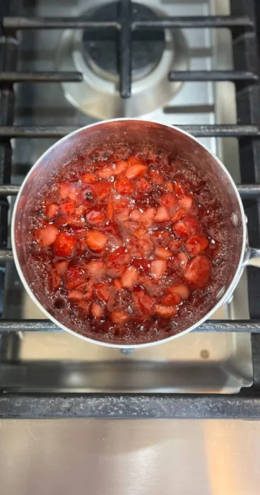 A pot of bubbling gluten-free strawberry sauce that is thickening on a stovetop.
