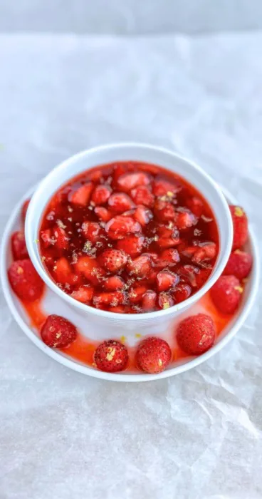 A vibrant red bowl filled with luscious gluten-free strawberry sauce, garnished with fresh sliced strawberries on the side.