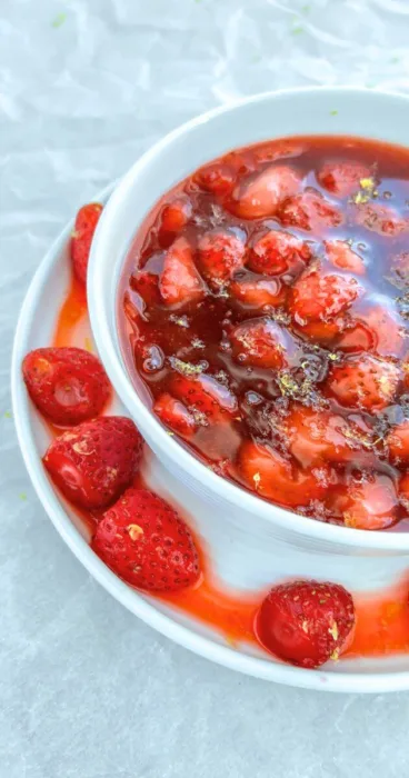 A close up of strawberries beside a bowl of smooth, glossy gluten-free strawberry sauce, ready to be drizzled over desserts or breakfast items.