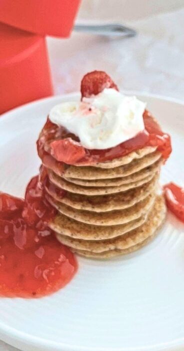 Golden-brown gluten-free sourdough discard pancakes with strawberry sauce piled on a plate.