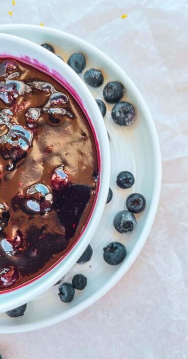 Close up of a bowl of blueberry topping  that's gluten free and dairy free surrounded by fresh berries.