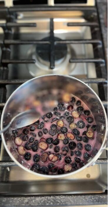 Pan with frozen blueberries being cooked into a thick blueberry topping.