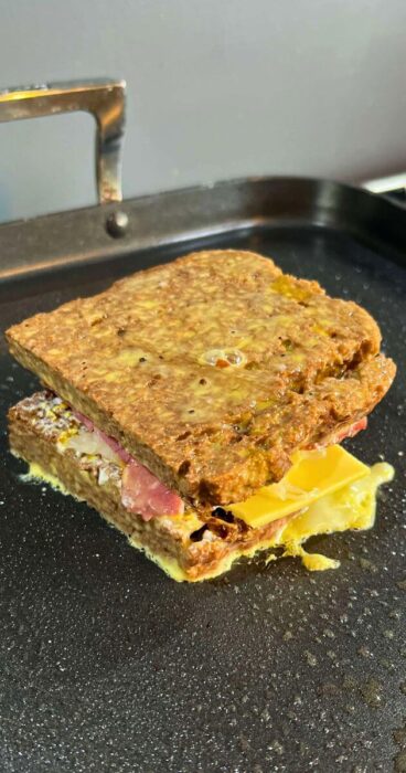 A gluten-free Reuben Monte Cristo sandwich being fried in a skillet, halfway through the cooking process.
