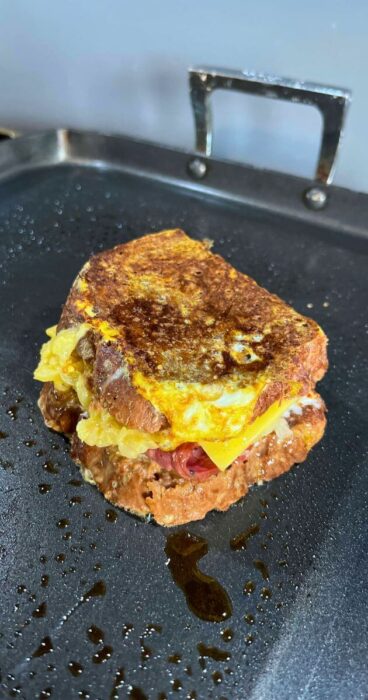 A gluten-free Monte Cristo sandwich being fried on a skillet, finishing the cooking process with melted cheese oozing out.