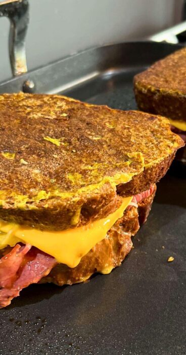 A skillet with sizzling gluten-free Reuben Monte Cristo sandwiches, cooking to a perfect golden brown.