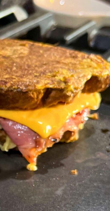 Side view of a Celiac friendly grilled Reuben Monte Cristo sandwich with melted cheese dripping out.