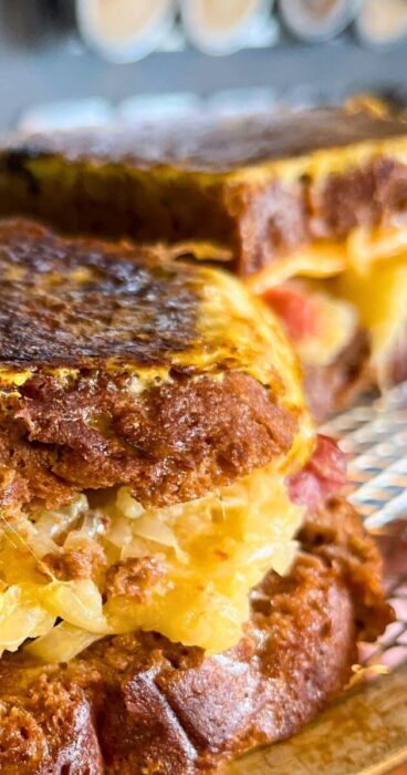 A close-up of a gluten-free Reuben Monte Cristo sandwich, golden brown and showing layers of corned beef, melted cheese, and sauerkraut.