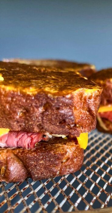 Close-up of the golden-brown crust of a gluten-free Reuben Monte Cristo sandwich, with melted cheese oozing out.