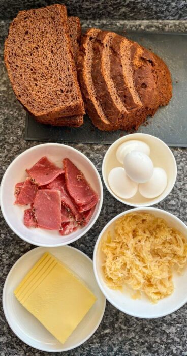 Ingredients for the gluten-free Reuben Monte Cristo sandwich laid out: gluten-free bread, smoked meat, cheese, sauerkraut, and eggs for egg batter.