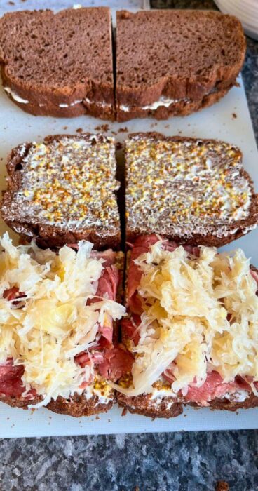 Two halves of a gluten-free Reuben Monte Cristo sandwich on a cutting board, showcasing the hearty layers inside.