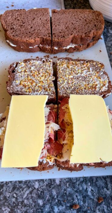 The sandwich assembly process revealing the layers of meat, plant-based cheese, Dijon mustard and sauerkraut.