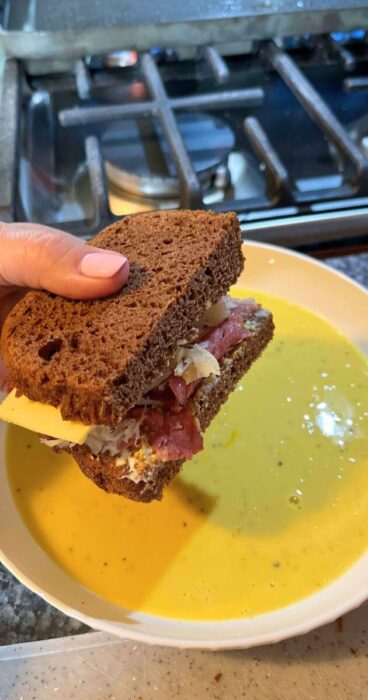 A gluten-free Reuben Monte Cristo sandwich placed being dipped in an egg batter.