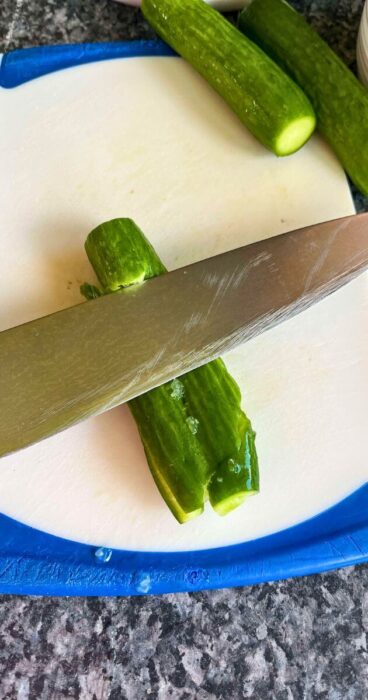 smashing cucumbers with a large knife for a mouthwatering gluten-free cucumber salad featuring aromatic dill