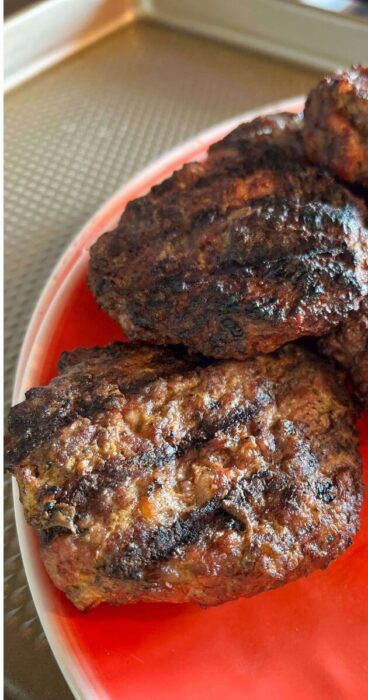 grilled gluten-free beef bacon burger patties on a plate, no bun.