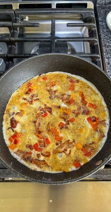 eggs, bacon, peppers, and onions in a skillet for an omelet breakfast wrap