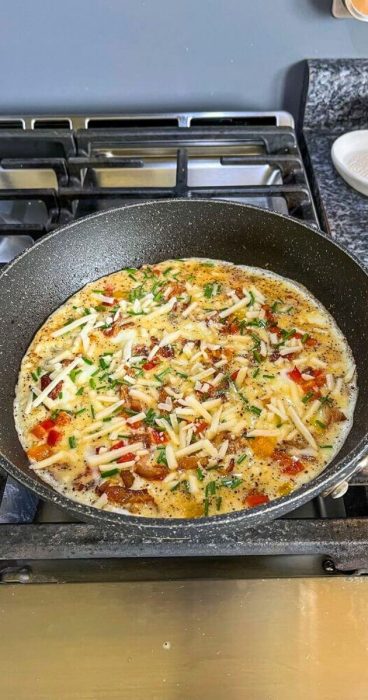 cheese and herbs on a fluffy omelet in a skillet for the gluten-free tortilla breakfast wrap